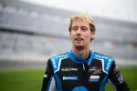 Race car driver in Acura racing suit at the track with blurred grandstands in the background