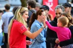 Smiling woman in red shirt high-fives toddler wearing pink among a crowd at an outdoor event.