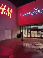 Person using long pole to maintain lights at Grapevine Mills mall entrance near H&M store at night.