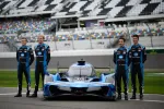Four race car drivers in black and blue suits standing next to a blue Acura race car on a racing track.