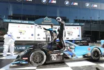 Race car with number 10 in victory lane as driver celebrates on car roof and another holds checkered flag