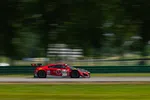 Red race car number 93 speeding on a racetrack with blurred green trees and grass background