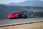 Red race car speeding on track with mountains and clear sky in background during daytime.