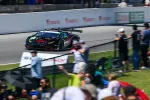 Black and green race car speeding on track with blurred spectators watching in foreground and barriers in background