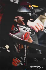 Close-up of a race car driver wearing a helmet and safety harness inside a racing car cockpit.