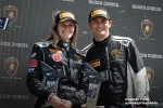 Smiling male and female race car drivers holding trophies on podium with Lamborghini and Roger Dubuis logos