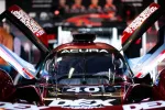 Front view of Acura race car with raised doors and team crew blurred in background.