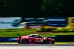 Red race car number 93 speeding on a racetrack with blurred background and sponsor logos