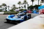 Blue Acura race car number 10 driving on track with palm trees and advertising banners in background.