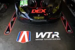 Front view of Wayne Taylor Racing IMSA race car with DEX branding in the garage with team logos on floor.