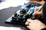Close-up of a hand detailing a black and blue model race car on a black surface with a marker pen.