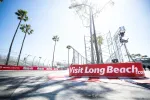 Wide view of a sunny Long Beach race track corner with palm trees and Visit Long Beach banner in foreground.