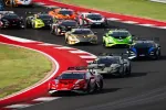 Race cars in various colors speed through a sharp turn on a professional racetrack during a competitive event