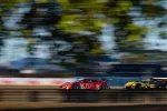 Red and yellow race cars speeding side by side on a blurred racetrack with trees and barriers in the background