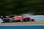 Red and black race car number 40 speeding on a racetrack with blurred background and blue barriers.