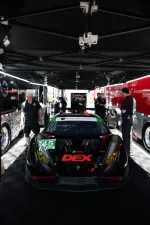 Black Lamborghini race car with DEX branding under tent surrounded by team members in a garage area.