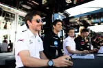 Smiling race drivers in team uniforms sitting at a table during a motorsport event autograph session.