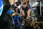 Two mechanics working on a blue race car engine in a professional garage with Konica Minolta branding
