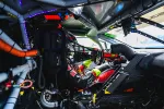 Race car driver in helmet and gloves inside high-tech vehicle cockpit preparing to drive on track.