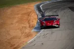 Red race car with aerodynamic design speeding on a racetrack corner with dirt beside the asphalt.