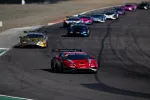 Red sports car leads a pack of race cars on a curving asphalt track during a competitive race.