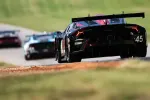 Race cars speeding on a track with a black car marked 45 leading the pack on a sunny day.
