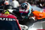Race car driver wearing a blue and pink helmet cleaning the windshield of a red car during a race event