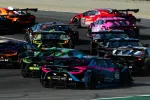 Multiple colorful Lamborghini race cars competing on a racetrack during a high-speed race turn.