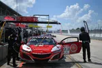 Red Acura NSX race car 93 in pit stop with crew refueling and preparing under sunny sky.