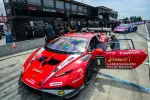 Red Lamborghini Huracán GT3 race car with open door at pit lane during motorsport event.