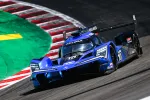 Blue Acura Konica Minolta race car with LED headlights speeding on a curved racetrack corner.