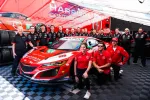 Racing team posing with red Acura NSX GT3 race car and Harrison Contracting trailer in background.