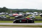 Black and red race car number 45 speeds on track with blurred background of spectators and vehicles.