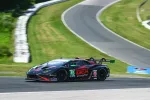 Black and red Lamborghini race car number 45 speeding on a curved racetrack with green grass surroundings.