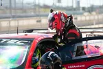 Race car driver in red helmet and suit entering a red and black #AllAndretti race car at the track.