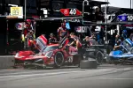 Red Acura race car number 40 in pit stop with crew members changing tires at professional motorsport event