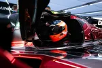 Race car driver wearing a helmet with stars and stripes sitting in a sleek black and red Acura race car.