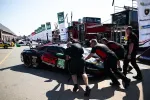 Race team pushes black and red number 45 sports car in paddock during motorsport event.