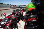Racing team members in black and red DEX Imaging uniforms preparing near a red Acura Type S race car at pit stop.