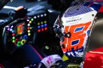 Race car driver wearing a colorful helmet inside a high-tech cockpit with illuminated steering wheel controls.