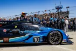 Blue and black race car number 10 on the track with pit crew and fans in background under clear sky
