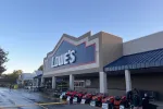 Lowe's home improvement store exterior with lawn mowers displayed in front under clear sky.