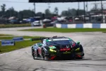 Black racing car number 45 with green headlights and red accents speeds on a race track during the day.