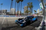 Black and blue race car speeding on Long Beach street circuit with city skyline and palm trees in background