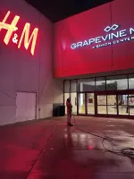 Person in red jacket holding a long pole under glowing H&M and Grapevine Mills mall signs at night.