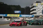 Red Acura race car leading multiple sports cars on a racetrack with Michelin banners and spectators in the background.