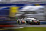Black and green race car speeding on racetrack with blurred background and sponsor logos visible.