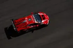 Aerial view of a red racing car speeding on a dark asphalt race track during daytime.
