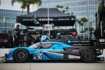 Konica Minolta Acura race car number 10 in pit lane with team members and equipment under branded canopy