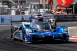 Blue Acura Konica Minolta race car speeding on a curving race track during a daytime event.